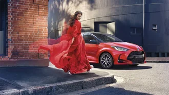 Roter Toyota Yaris und Model in wallendem roten Seidenkleid an einer Straßenecke