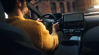 Blick über die Schulter einer Person am Steuer des Toyota bZ4X. Auf dem digitalen Dashboard ist ein Navigationsgerät zu sehen.