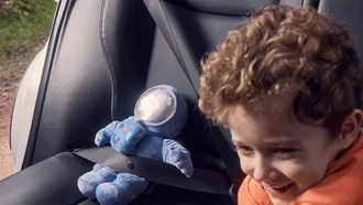 Nahaufnahme von einem Kindersitz im Toyota Corolla Cross. Auf dem Sitz ist ein Plüsch-Astronaut angeschnallt und daneben befindet sich ein freudiges Kind.