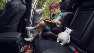 Innenansicht der Rücksitzbank des Toyota Corolla Cross. In einem Kindersitz ist ein Kind zu sehen, das bei offener Tür ein Buch liest und ein Eisbär-Stofftier neben sich hat.