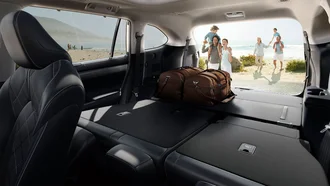 Blick vom Cockpit des Toyota Highlander aus dem Kofferraum, vor dem eine Großfamilie mit gEpäck vor einem Strand- und MEereshintergrund zu sehen ist