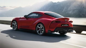 Roter Toyota Supra auf Küstenstraße mit See und Bergen im Hintergrund