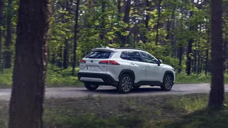 Der Toyota Corolla Cross fährt durch ein Waldstück. Das Fahrzeug ist dabei schräg von hinten zu sehen.