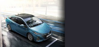 Erhöhte Schrägansicht auf die Vorderseite eines TOYOTA PRIUS Plugin Hybrid mit himmelblauem Lack. Der Neuwagen wurde auf einem Parkplatz in der Stadt am hellichten Tag geparkt. Ein drittel des Bildes wird mit einem grauen Balken überdeckt.