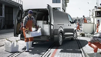 Grauer Toyota Proace neben einem Fischerboot. Neben dem Auto laufen Arbeiter mit Fischkörben rum