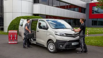 Grauer Toyota Proace im Profil mit offener Schiebetür, daneben zwei Arbeiter